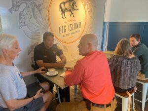 Three men and a woman sitting at a table in a coffee shop with a police officer. 