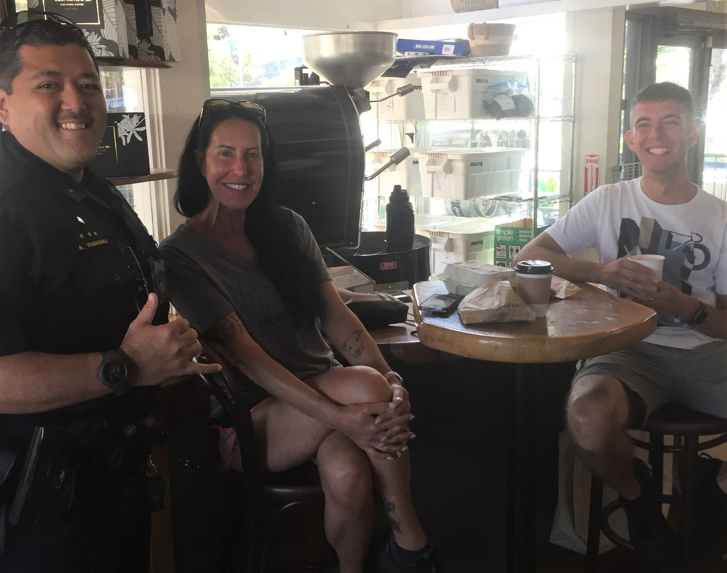 Officer and a man and woman at a coffee shop smiling for the camera at Coffee With a Cop