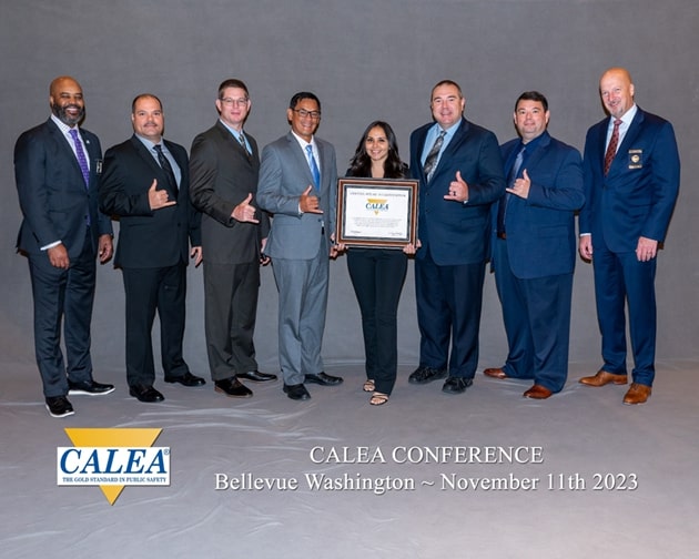 Group shot of 7 men and 1 woman holding a CALEA sign