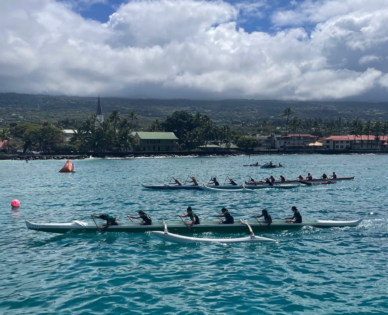 Outrigger canoes and paddlers racing in a regatta off the Kona shoreline.