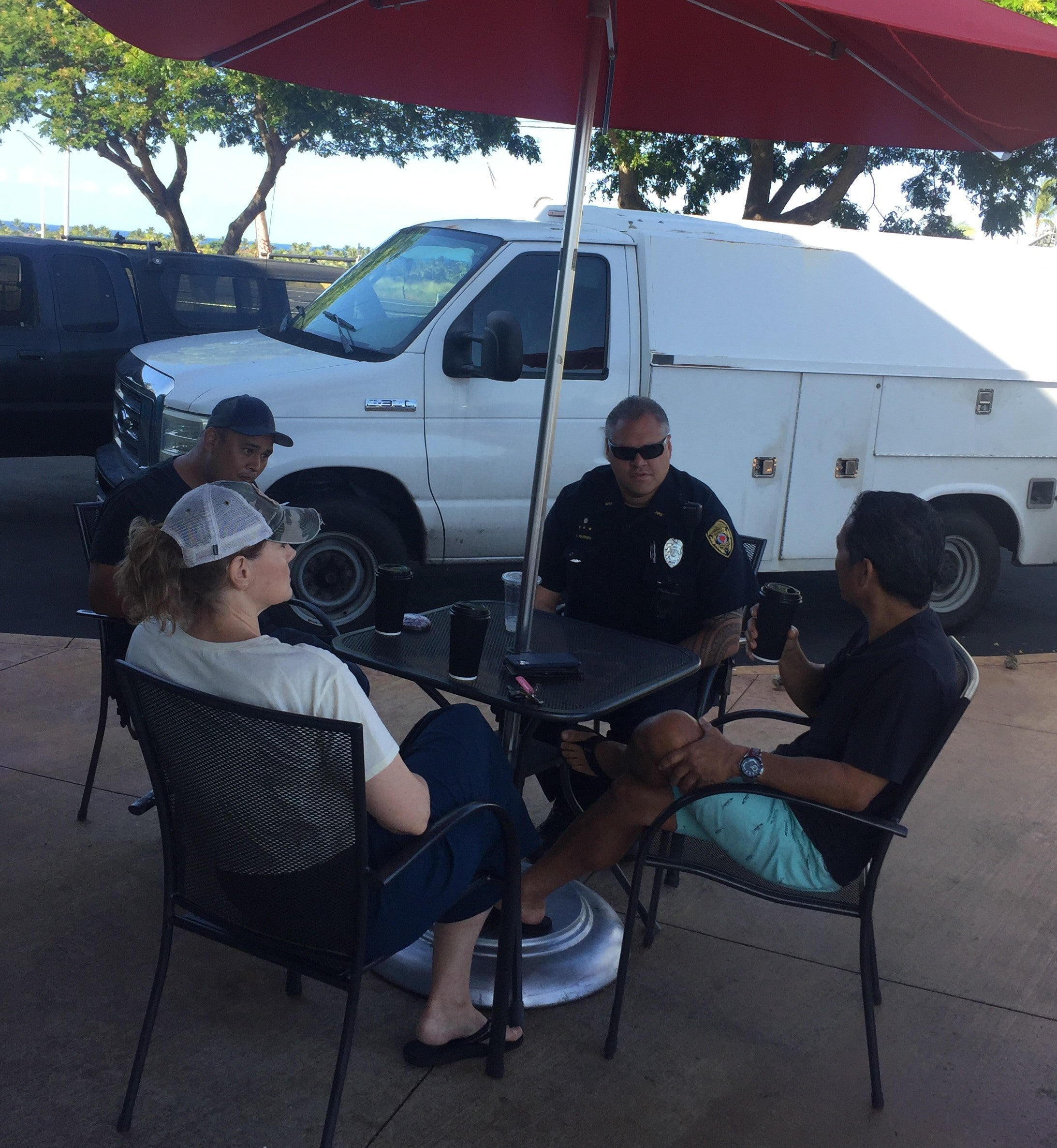 Officer seated at outdoor cafe table with three people.