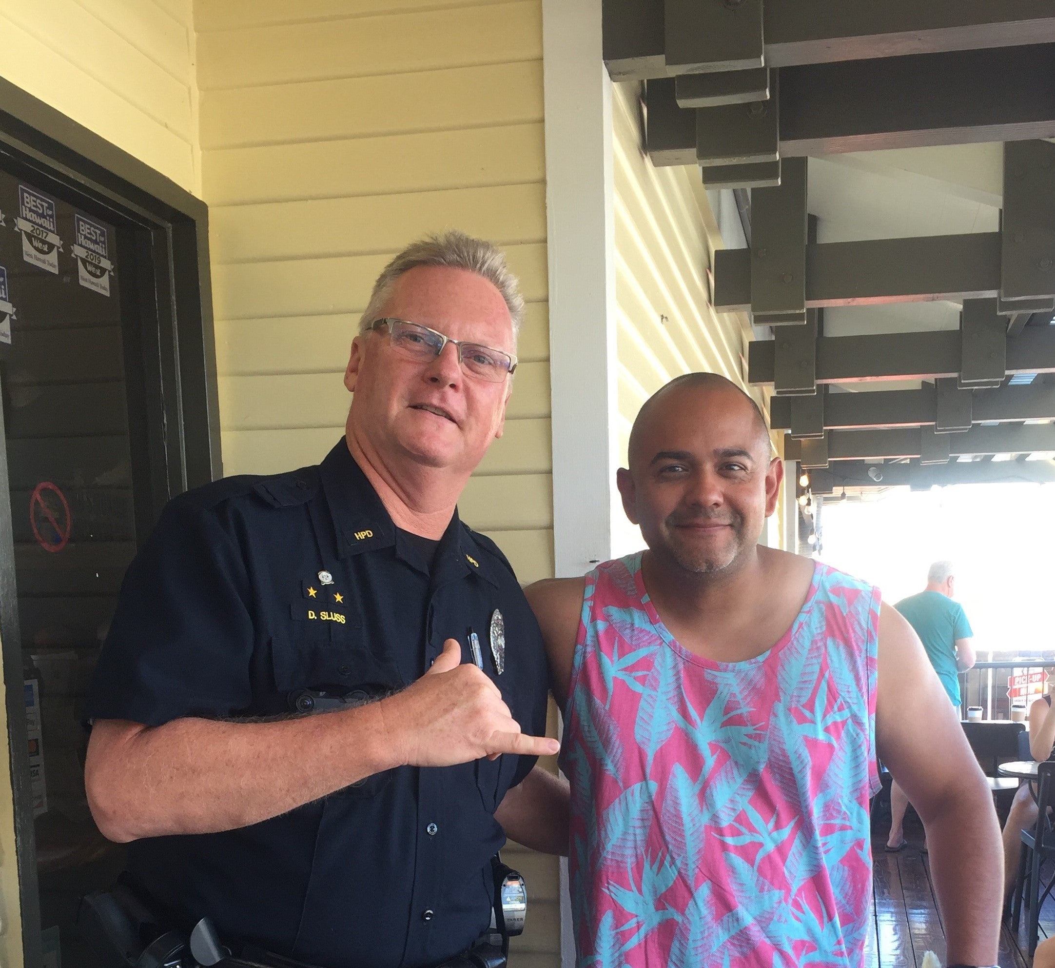 Officer and man smiling at camera outside coffee shop.