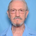 Photo of William Bishop Sr. with grey hair, blue eyes, and grey beard. He is wearing glasses and a blue shirt.