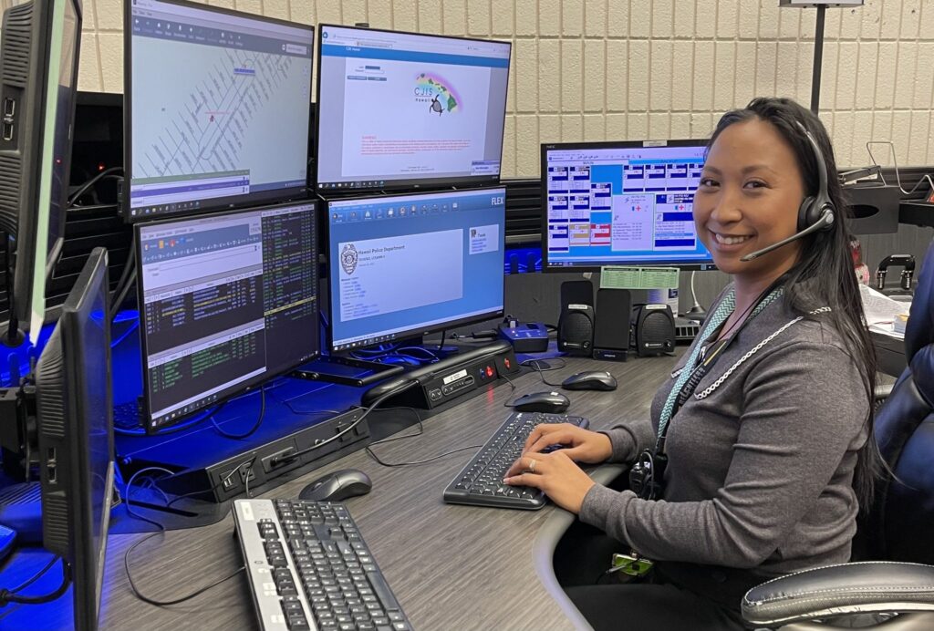 Police dispatcher sitting at desk in front of seven screens