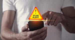 Man holding smartphone with the words scam alert above phone. 